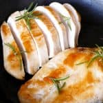 1 whole and one cut up Chicken Breast with rosemary in a cast iron pan with lemons in the background- Paint the Kitchen Red