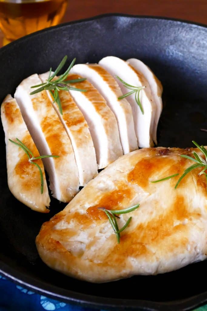 sous vide chicken breast: 1 whole and one cut up Chicken Breast with rosemary in a cast iron pan with lemons in the background- Paint the Kitchen Red
