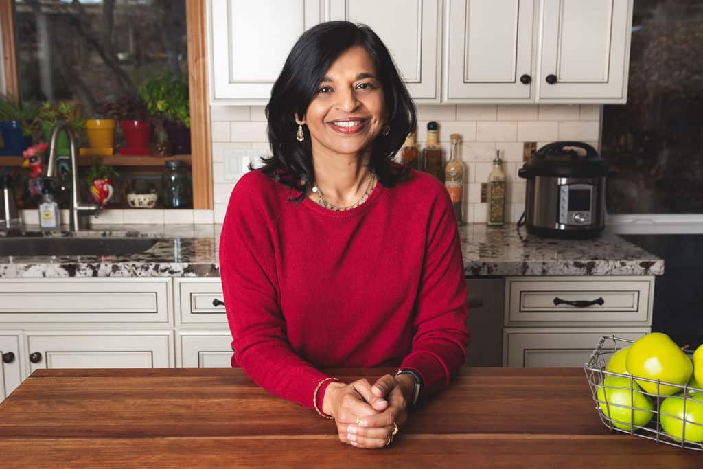 Neena in red sweater in a white kitchen leaning on the counter - Paint the Kitchen Red