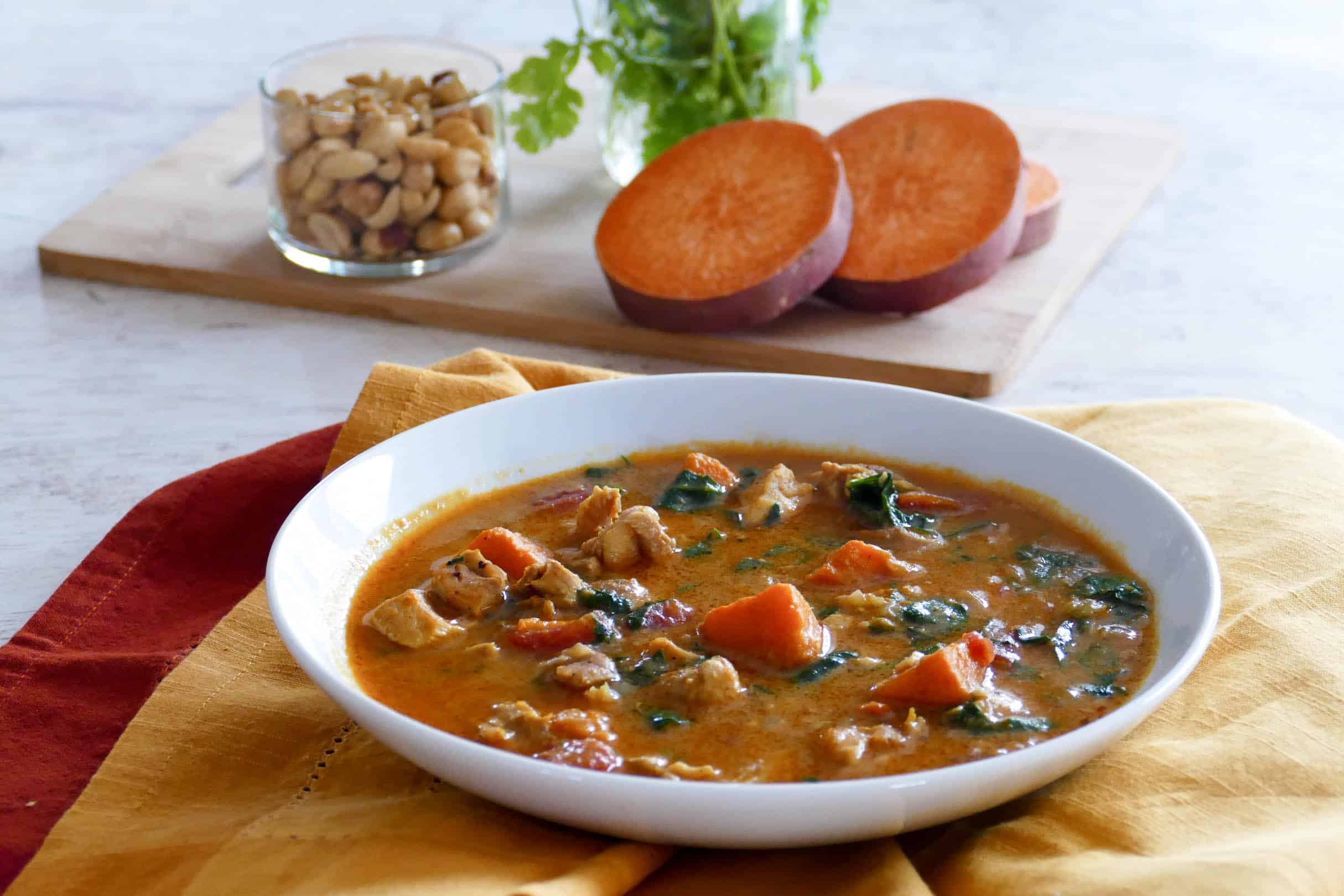 Instant Pot African Peanut Stew in a white bowl with cut sweet potato, peanuts and cilantro in background