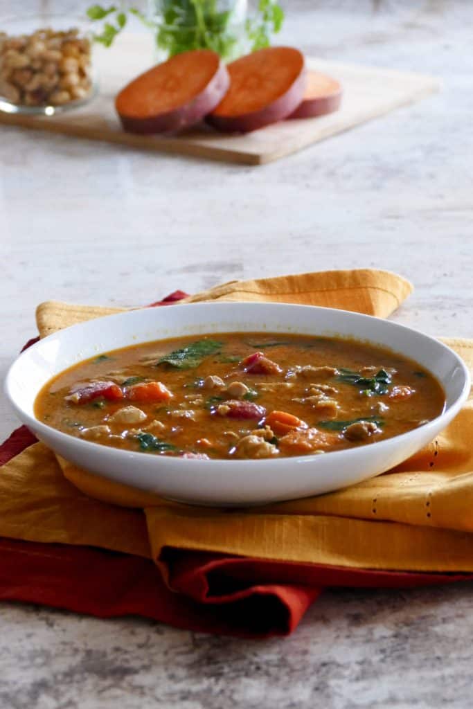 Instant Pot African Peanut Stew in a white bowl with cut sweet potato, peanuts and cilantro in background