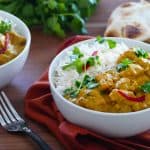 Instant Pot chicken korma curry with rice in a bowl with naan bread in the background
