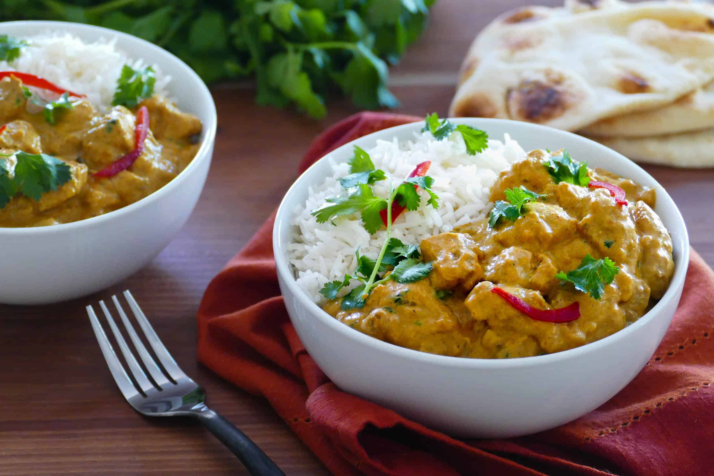 Instant Pot chicken korma curry with rice in a bowl with naan bread in the background