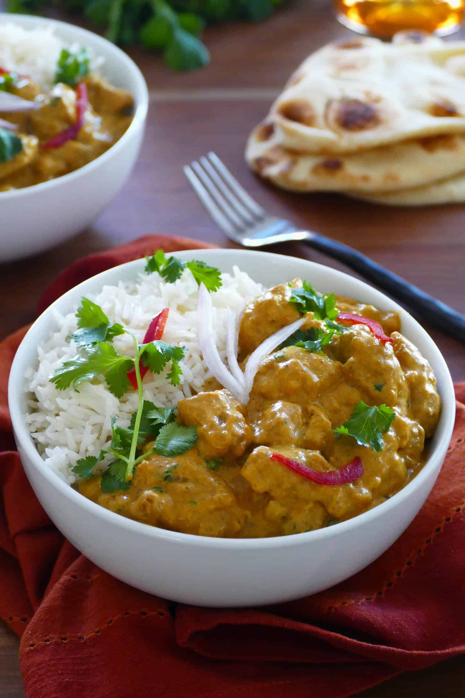 Instant Pot chicken korma curry with rice in a bowl with naan bread in the background