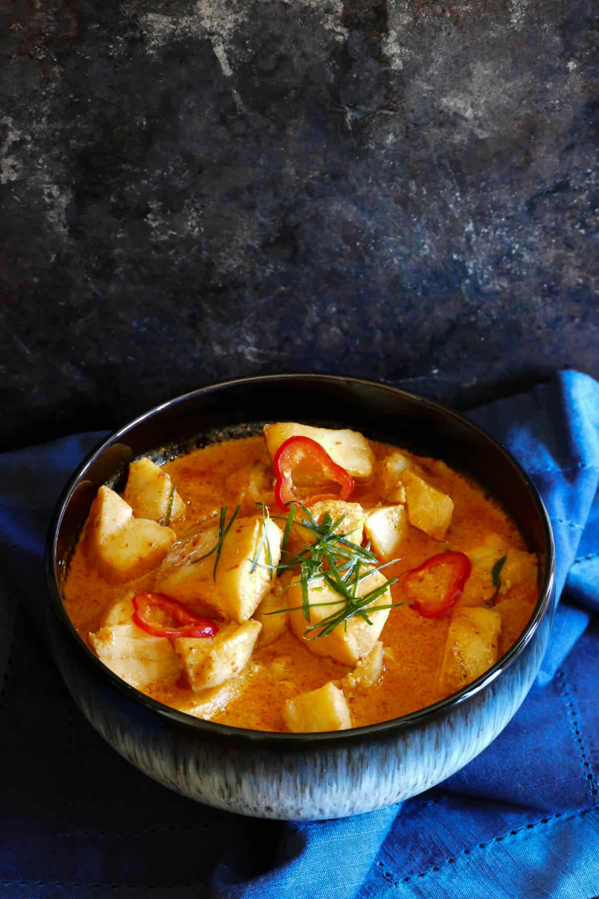 Instant Pot Fish Curry in blue bowl on blue napkin garnished with chili and red chili