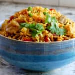 Blue bowl on counter with yellow rice, peas, chicken topped with cilantro