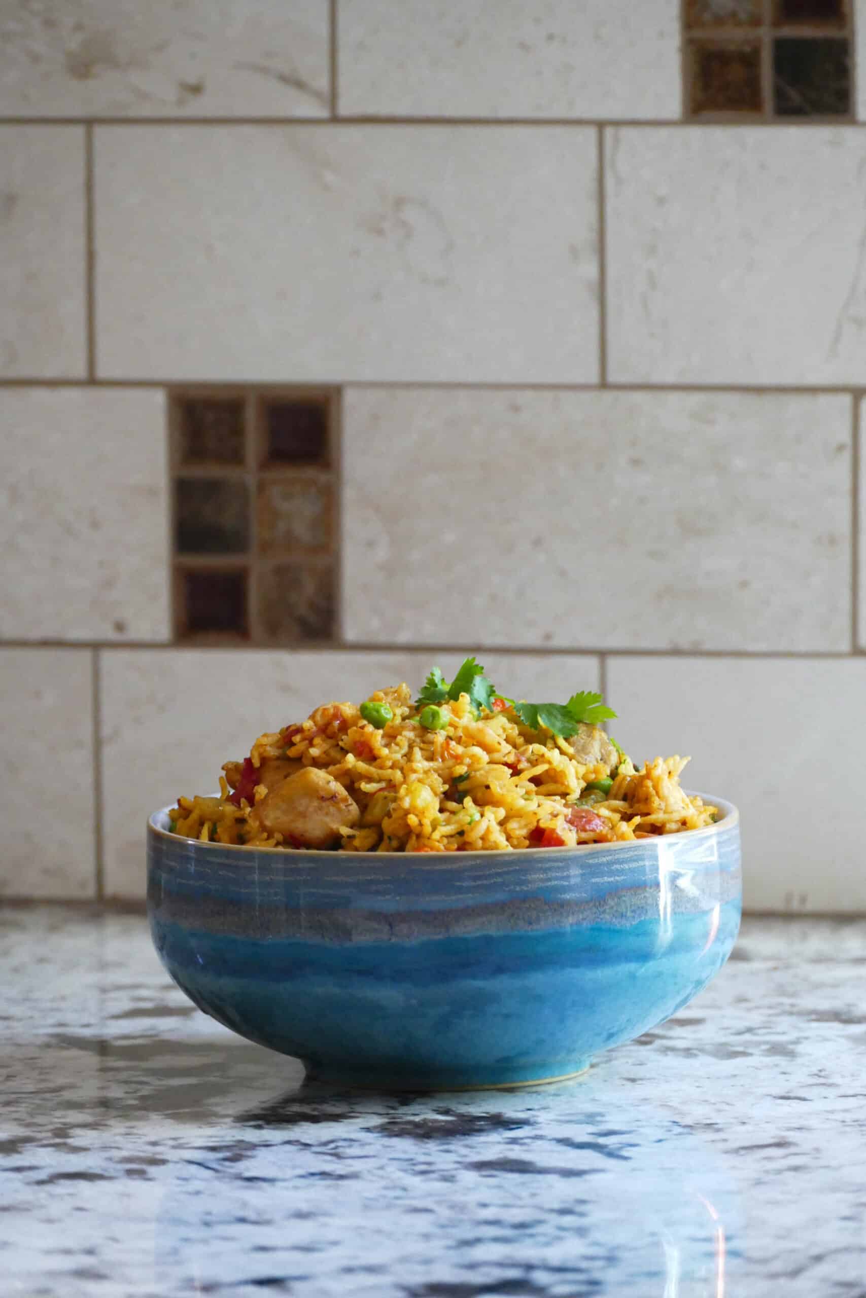 Instant Pot arroz con pollo - Blue bowl on counter with yellow rice, peas, chicken topped with cilantro