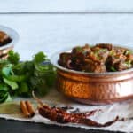 Instant Pot Rogan Josh in a copper dish with whole spices and cilantro in background