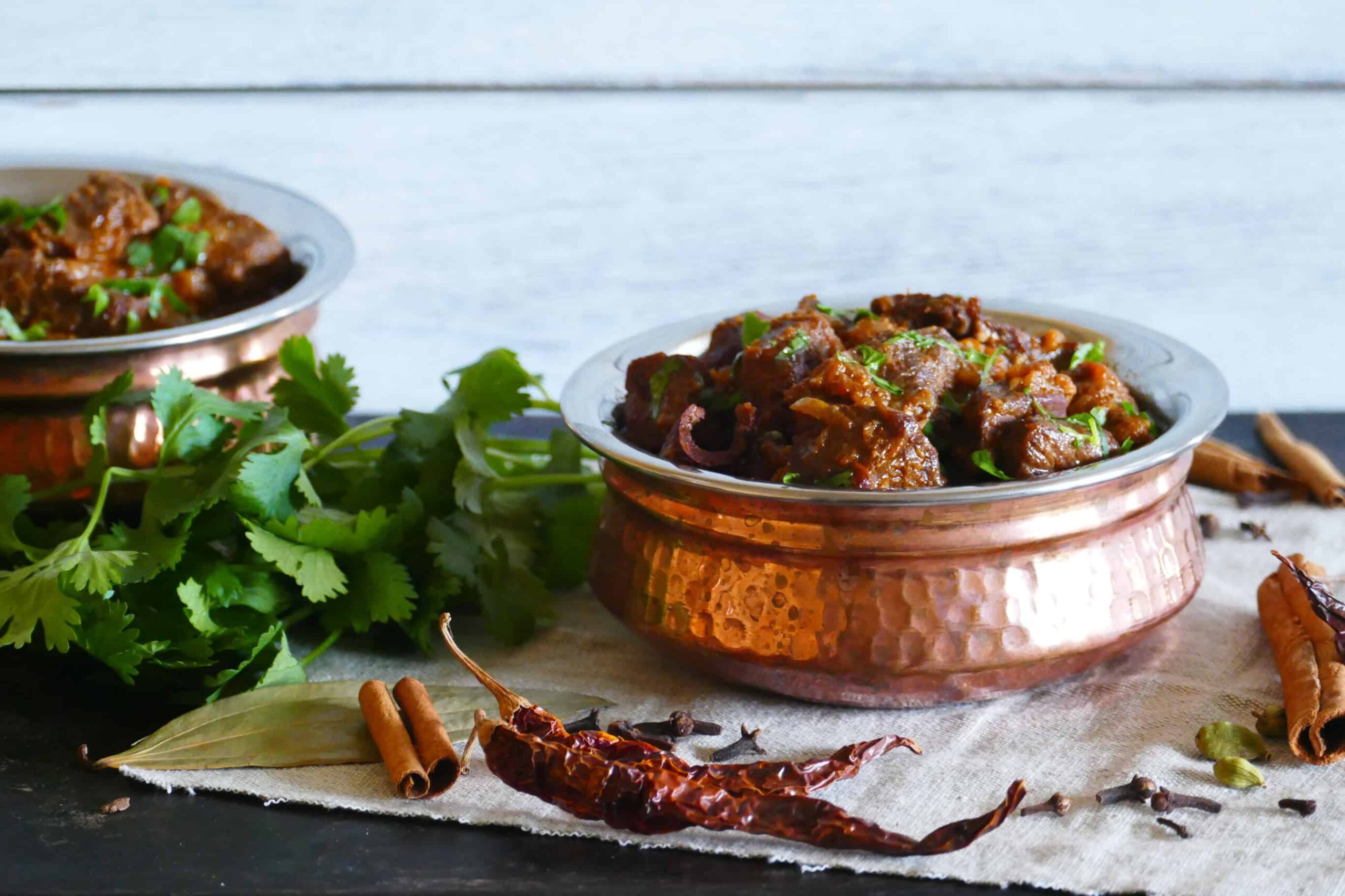 Instant Pot Rogan Josh in a copper dish with whole spices and cilantro in background