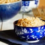 Parboiled brown rice in a blue bowl with a larger bowl of rice in background