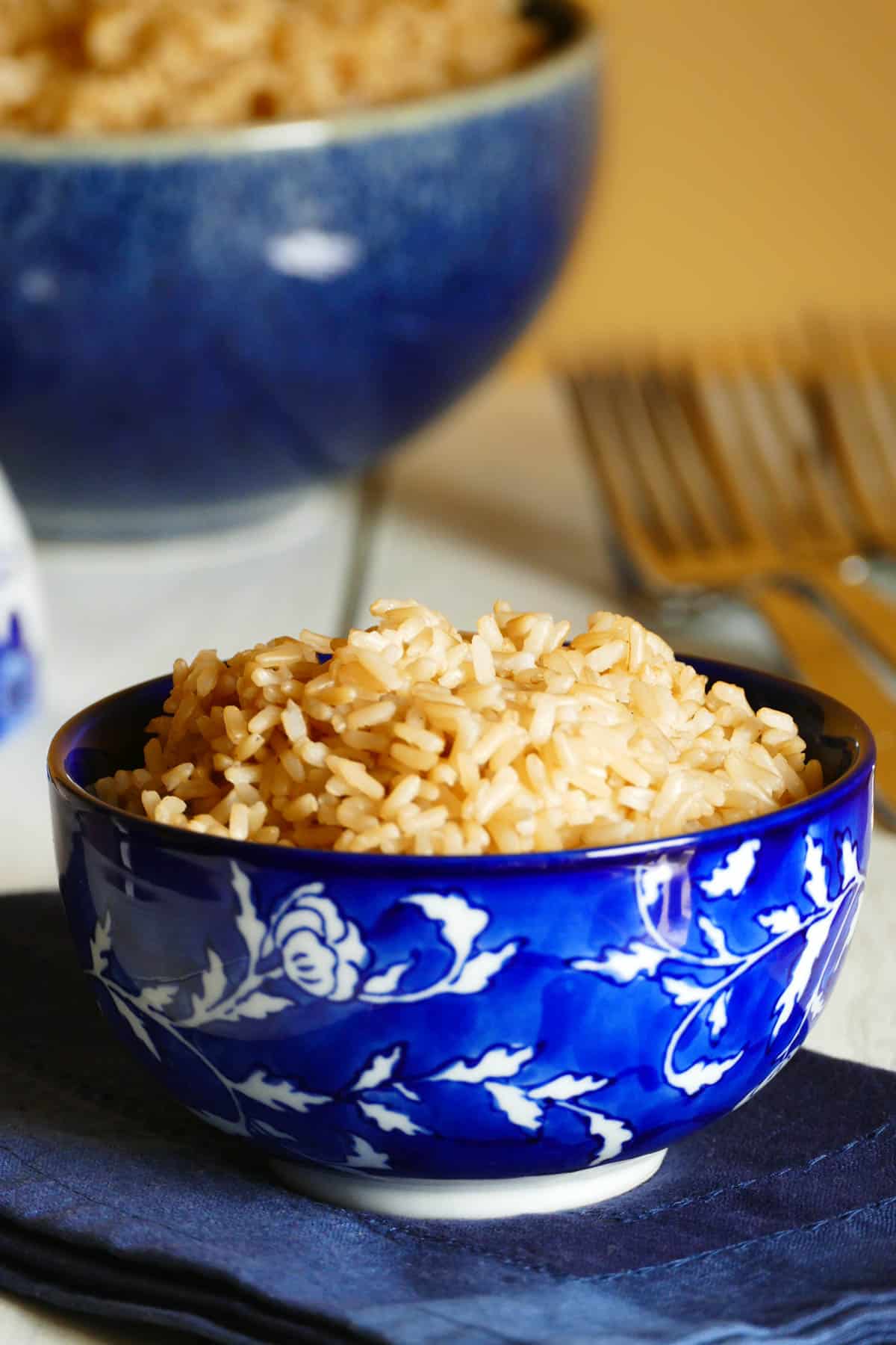 Parboiled brown rice in a blue bowl with a larger bowl of rice in background