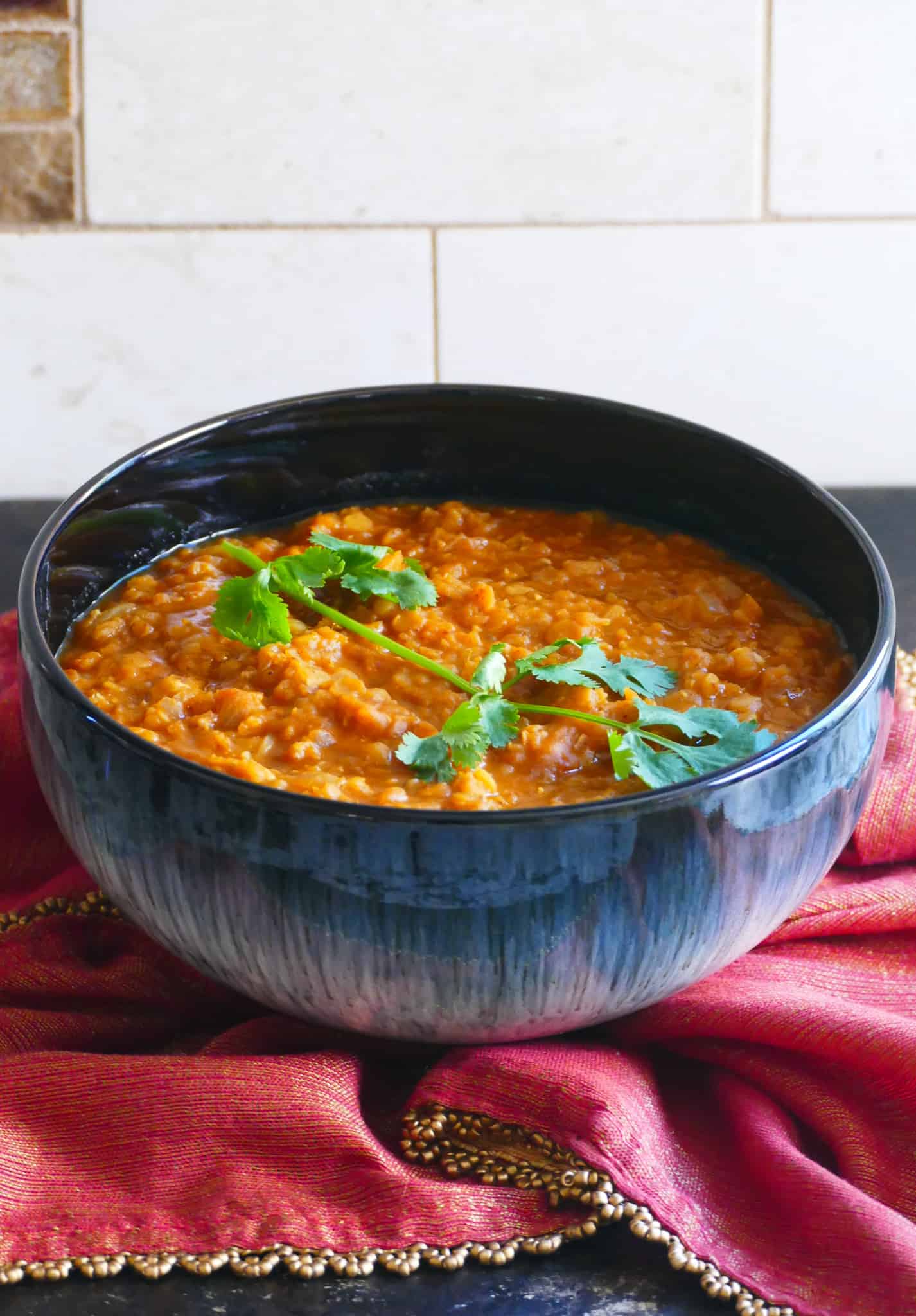 Blue bowl of orange red Ethiopian lentils garnished with cilantro on a red and gold napkin