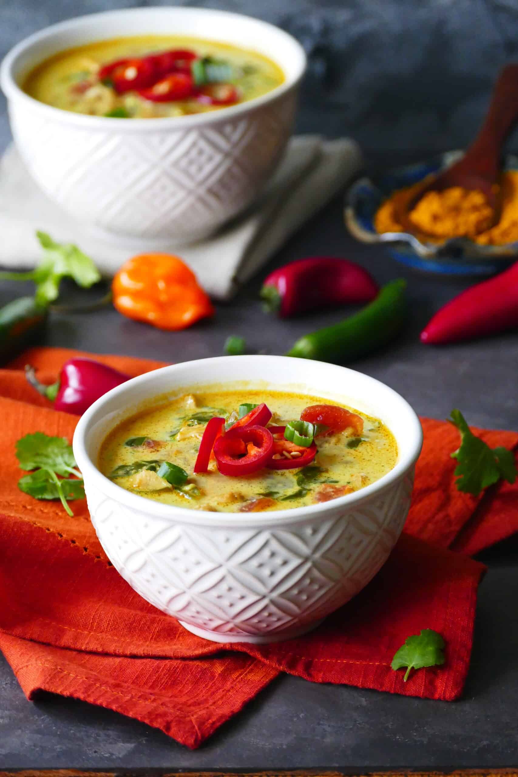 Chicken curry soup - Two white bowls of yellow colored soup garnished with red jalapenos and green onions on an orange napkin