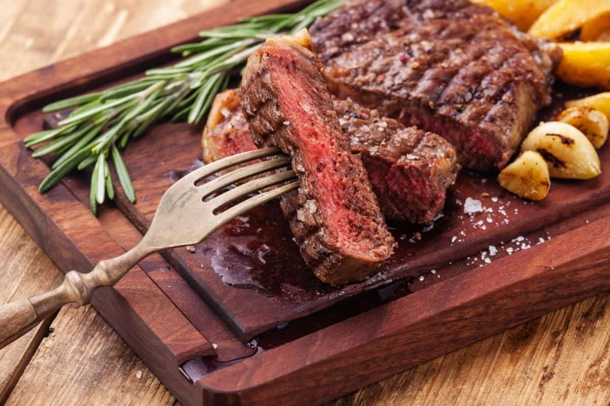 beef steak cut into slices with potaotes on a wooden board