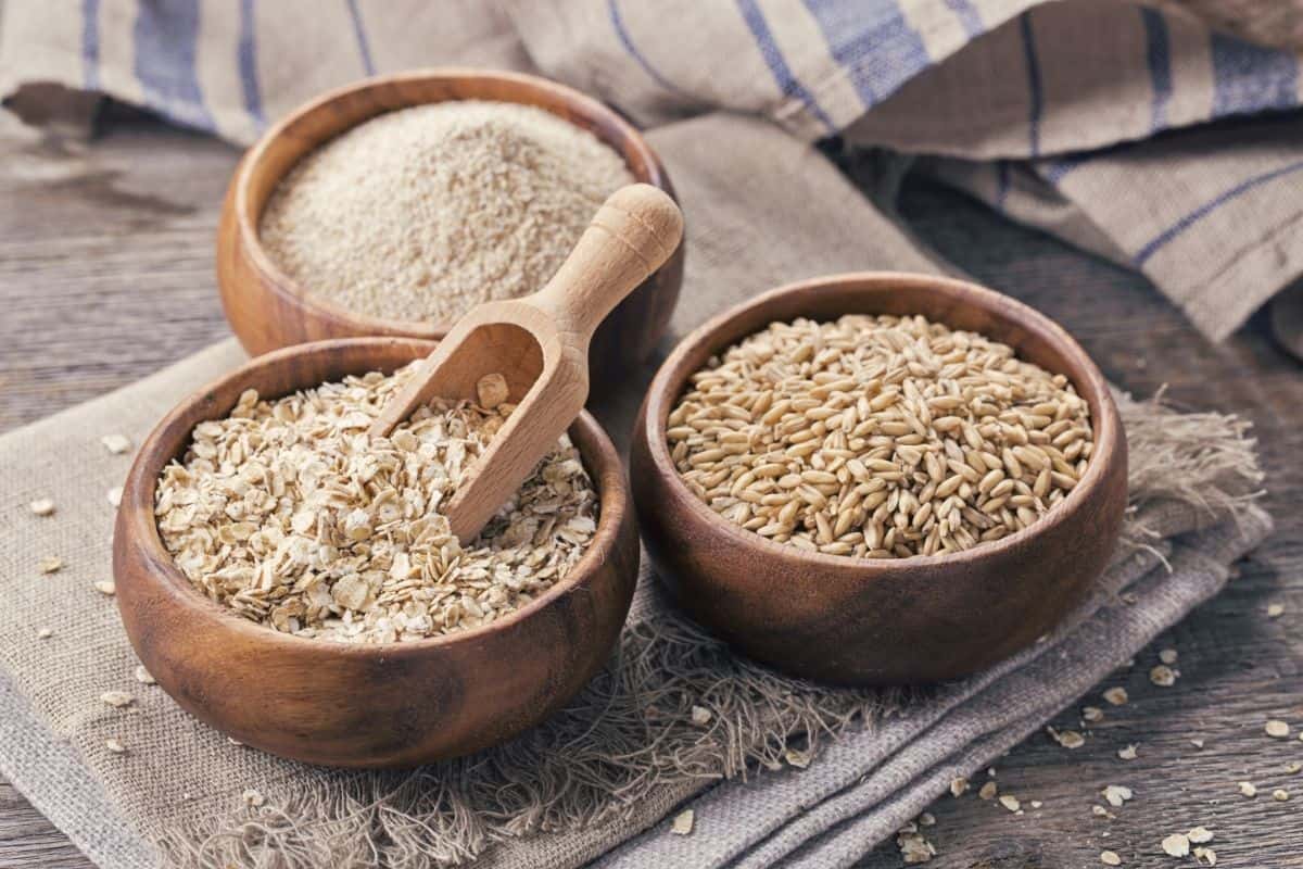 three wooden bowls on sack cloth with grains including oats