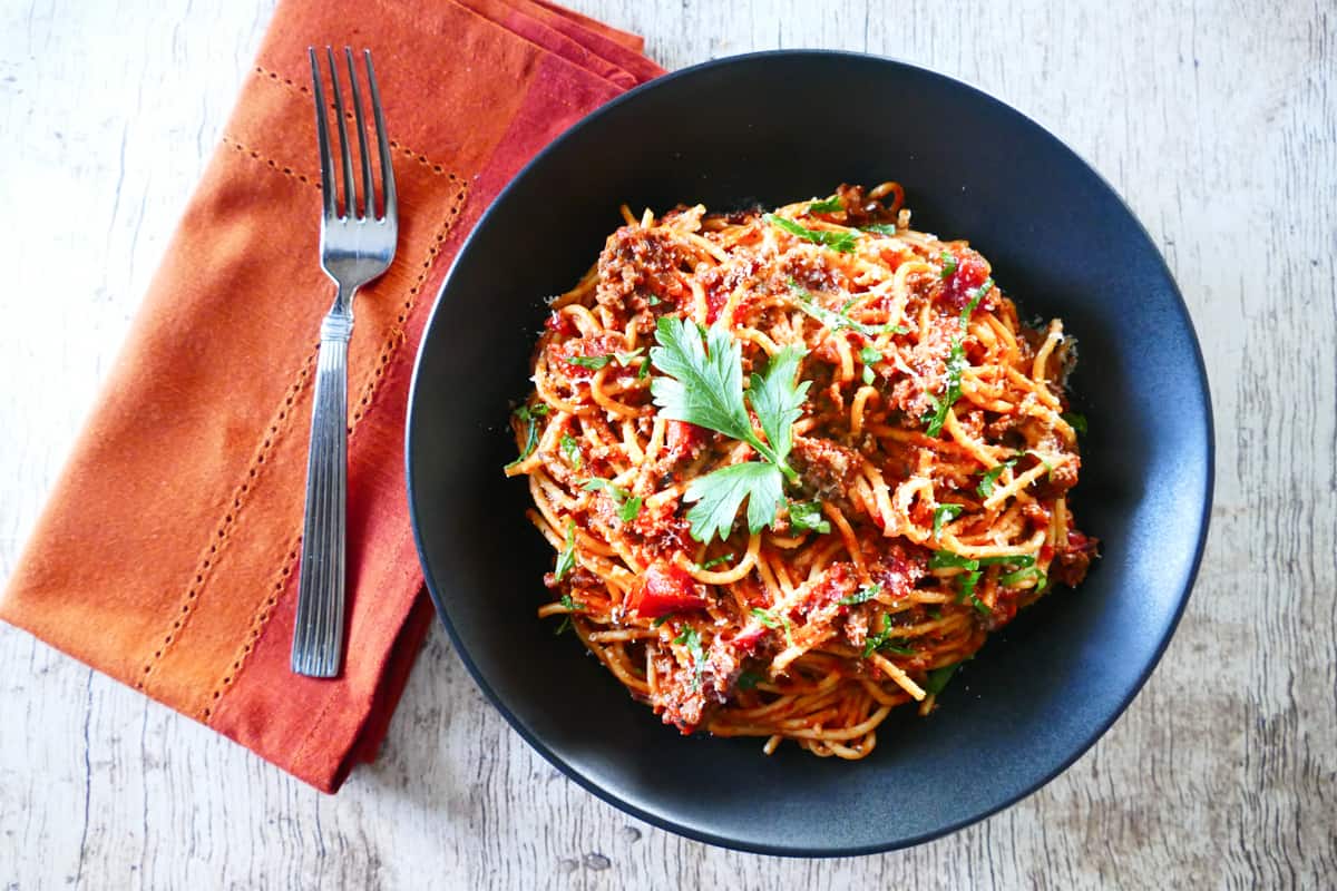 Instant Pot Spaghetti and Meat Sauce in a black bowl and wood background; napkin with bread on the side - Paint the Kitchen Red