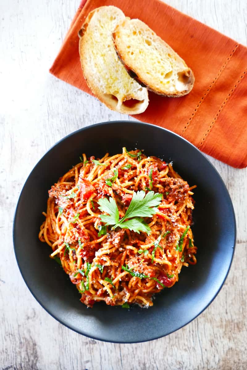 Instant Pot Spaghetti and Meat Sauce in a black bowl and wood background; napkin with bread on the side - Paint the Kitchen Red