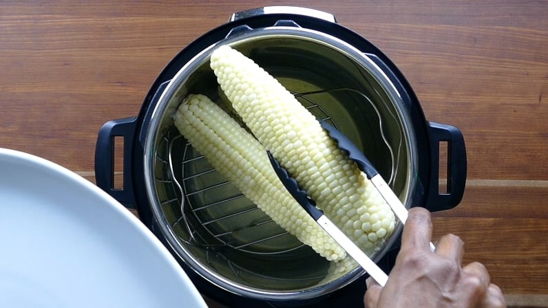 Corn on the cob being removed from Instant Pot with tongs