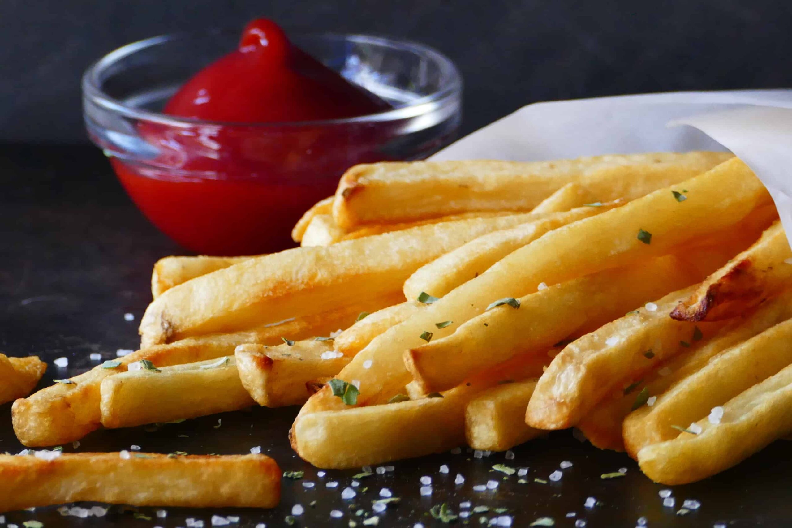 French fries with sea salt and parsley wrapped in white parchment and a glass bowl with ketchup