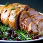Turkey breast partly sliced on a white platter with rosemary and cranberry garnish