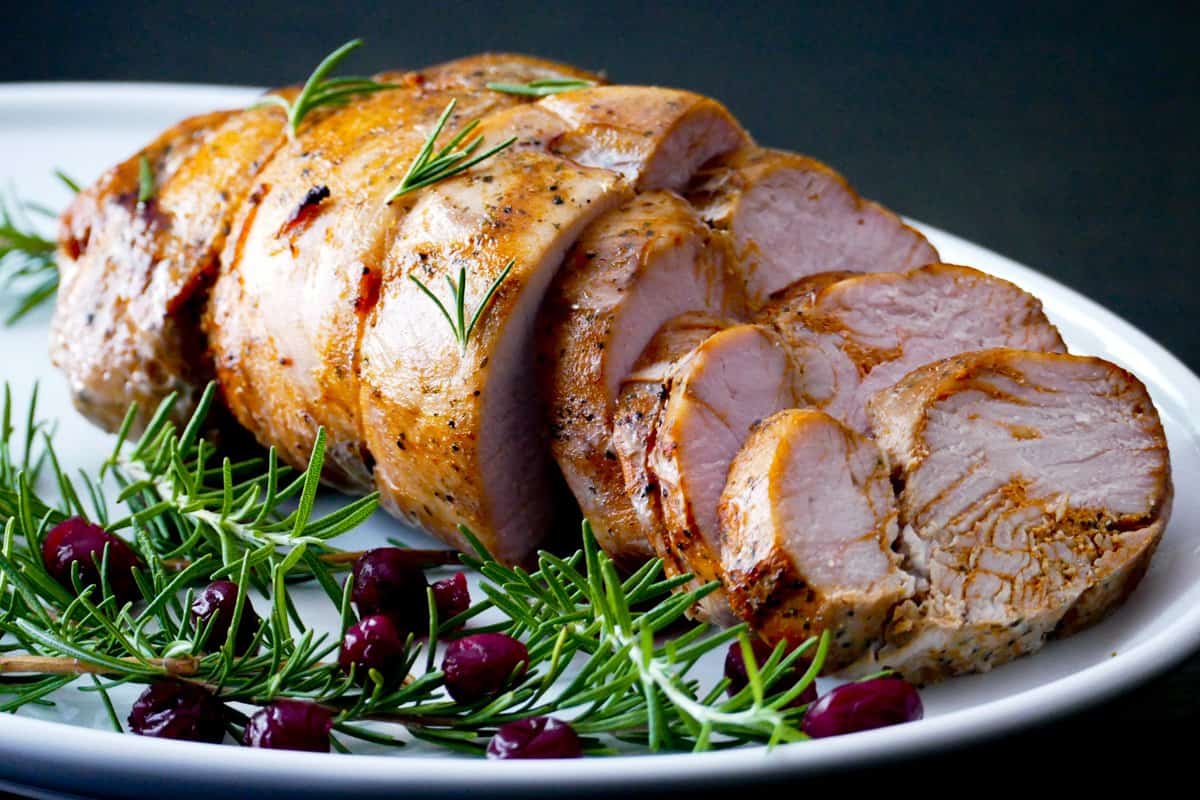 Turkey breast partly sliced on a white platter with rosemary and cranberry garnish