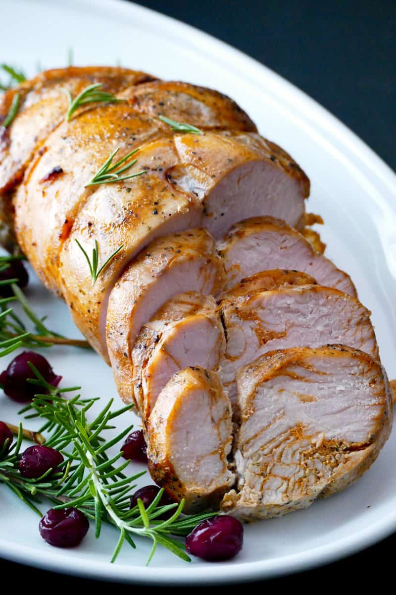 Sous vide turkey breast partly sliced on a white platter with rosemary and cranberry garnish