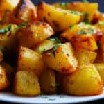 White plate with crispy golden potatoes stacked and garnished with parsley