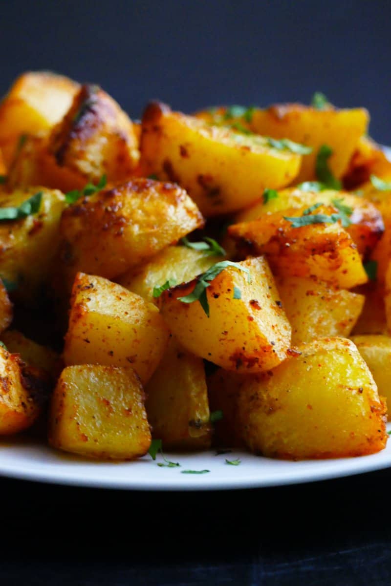 White plate with crispy golden potatoes stacked and garnished with parsley