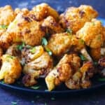 golden brown roasted cauliflower on a black plate with parsley garnish