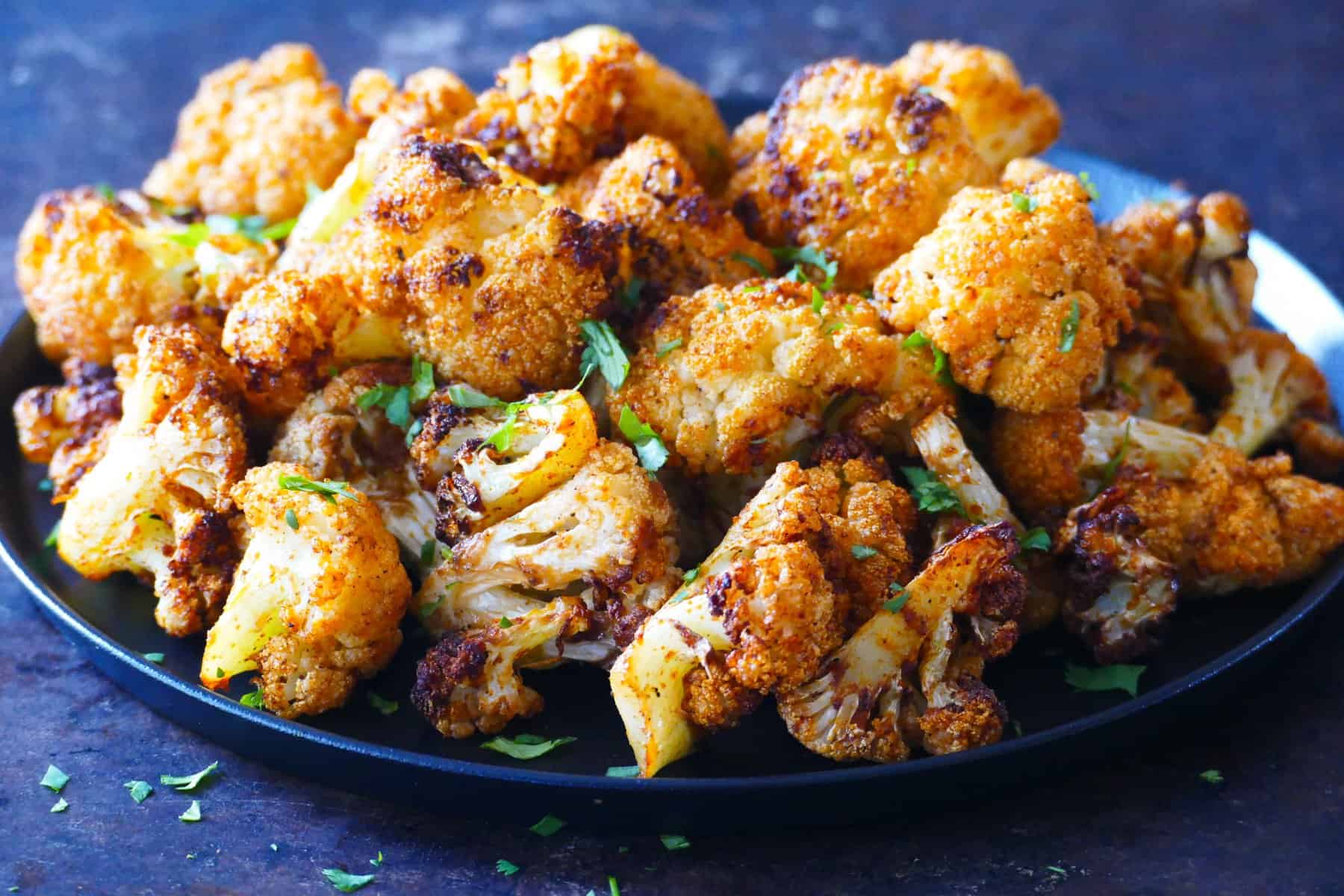 golden brown roasted cauliflower on a black plate with parsley garnish