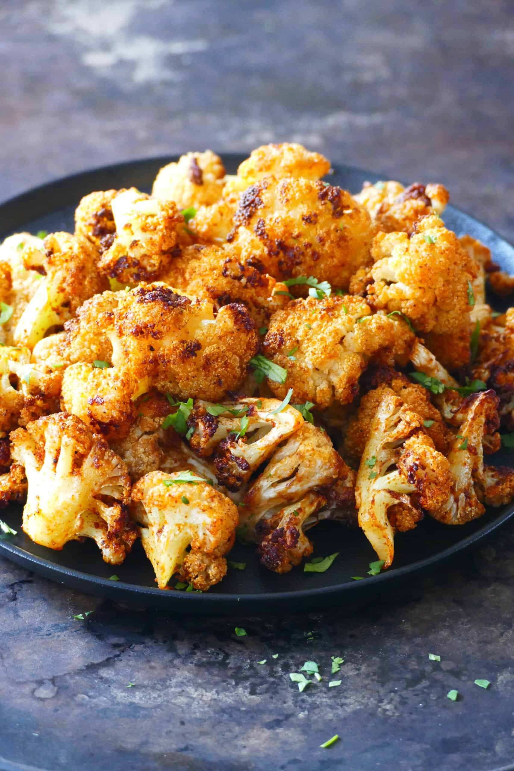 golden brown roasted cauliflower on a black plate with parsley garnish