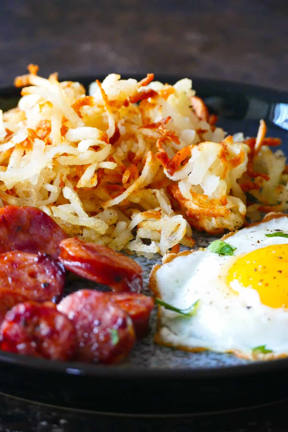 Air fryer frozen hashbrowns - Blue plate with golden brown shredded hashbrowns, fried egg and sliced sausage.