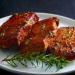 3 spice crusted pork chops on white plate with rosemary garnish