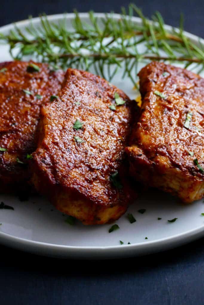 3 spice crusted pork chops on white plate with rosemary garnish