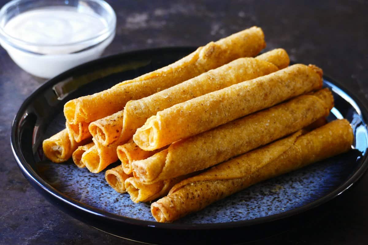 Rolled filled tortillas stacked on each other in a blue speckled platter