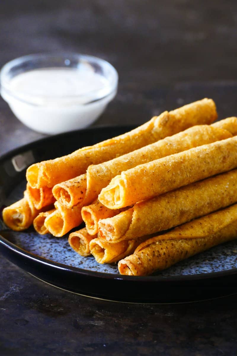 Frozen taquitos in air fryer - Rolled filled tortillas stacked on each other in a blue speckled platter