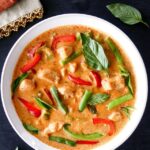 rich colored panang curry with vegetables and chicken garnished with Thai basil.