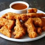 White plate with crispy golden chicken nuggets with red sauce in white bowl