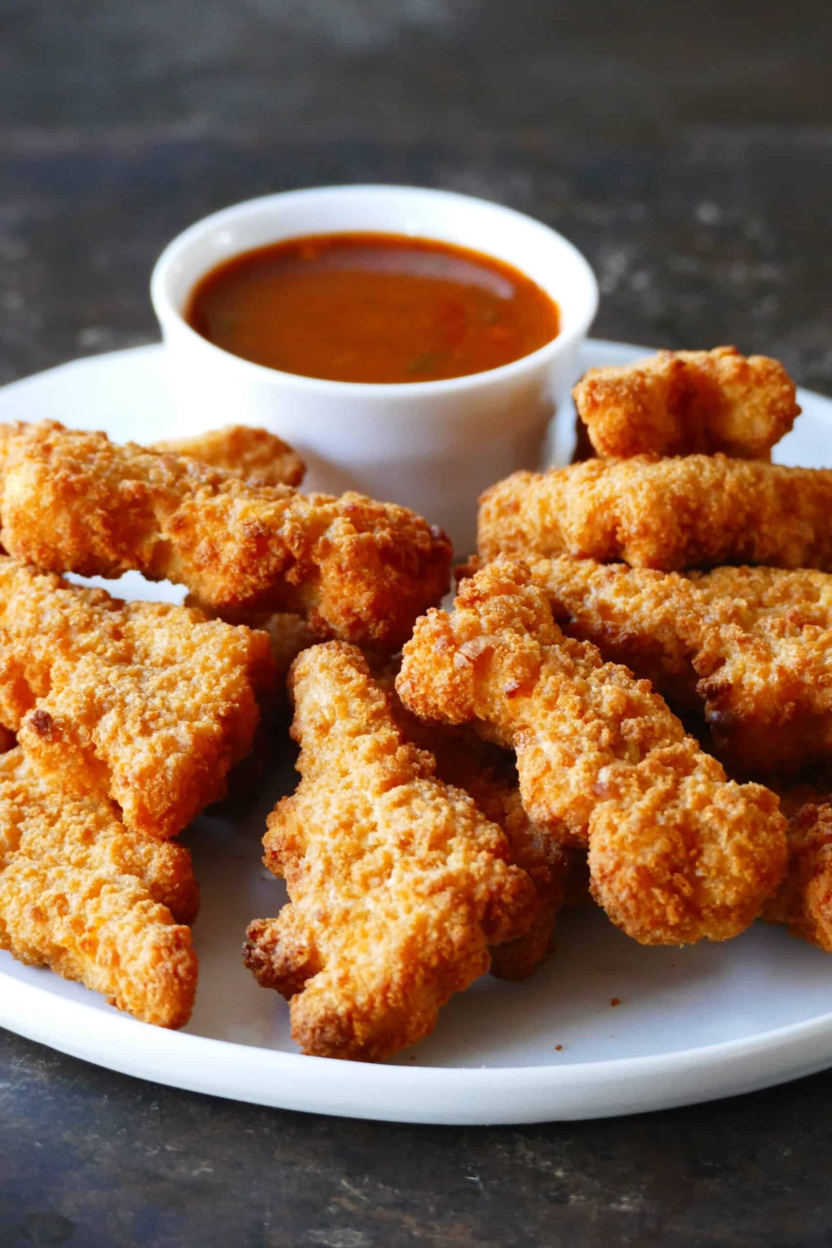 White plate with crispy golden chicken nuggets with red sauce in white bowl