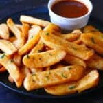 Black plate with steak fries garnished with parsley and bowl of red sauce