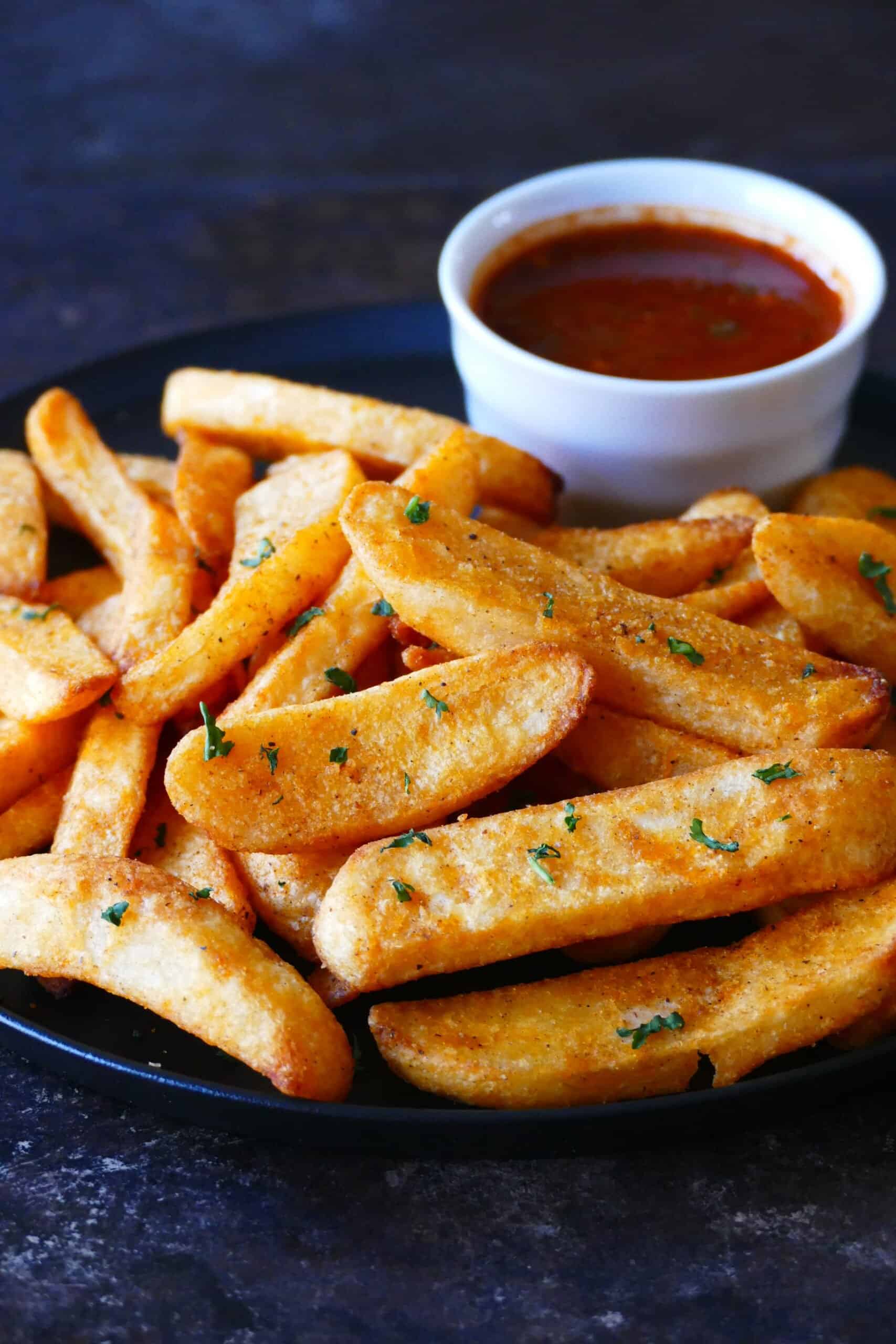 Air fryer frozen steak fries - Black plate with steak fries garnished with parsley and bowl of red sauce