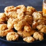 Black plate with crispy popcorn chicken with orange sauce in glass bowl