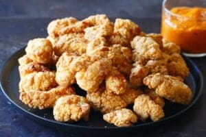 Black plate with crispy popcorn chicken with orange sauce in glass bowl