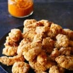 Black plate with crispy popcorn chicken with orange sauce in glass bowl