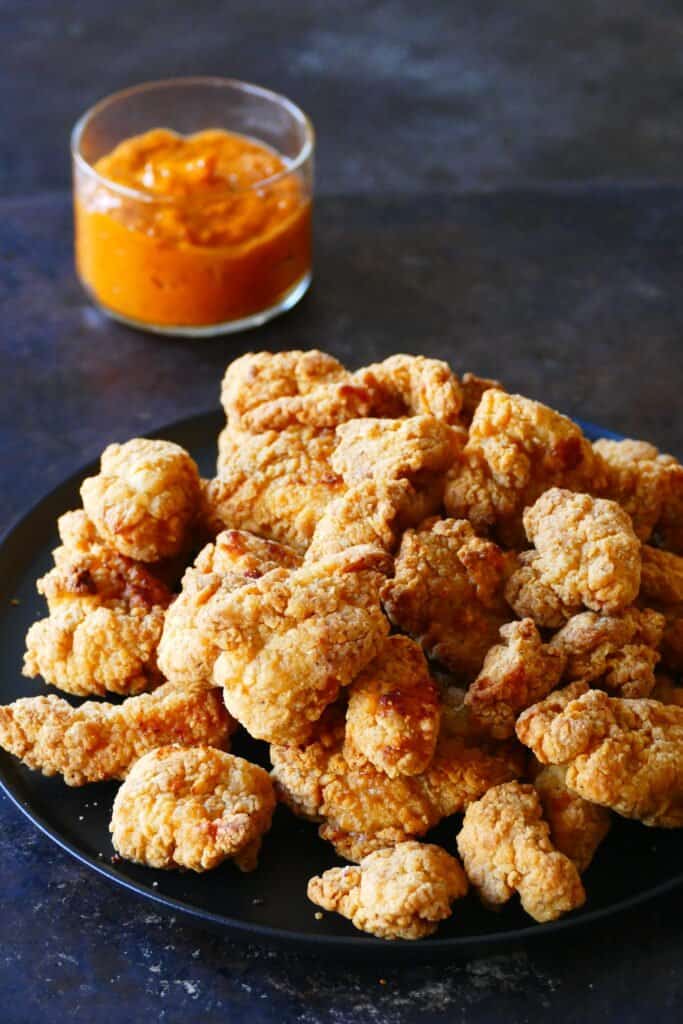 Black plate with crispy popcorn chicken with orange sauce in glass bowl