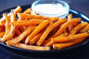 Black plate with sweet potato fries and bowl of white sauce