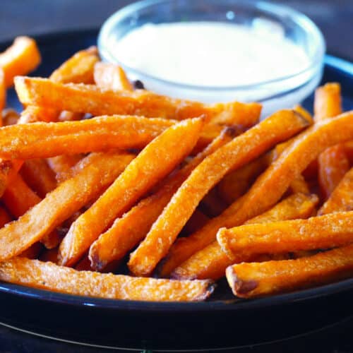 Black plate with sweet potato fries and bowl of white sauce