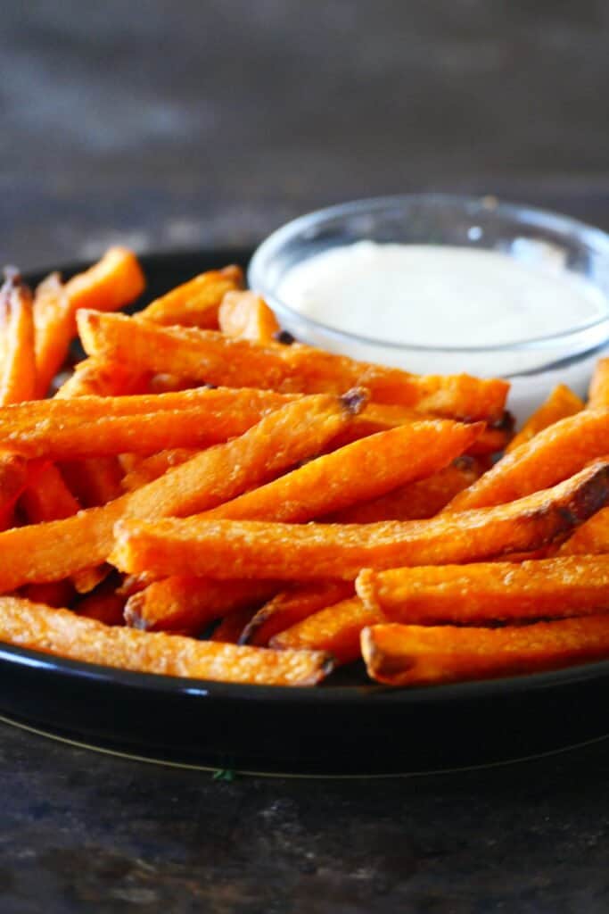 Black plate with sweet potato fries and bowl of white sauce