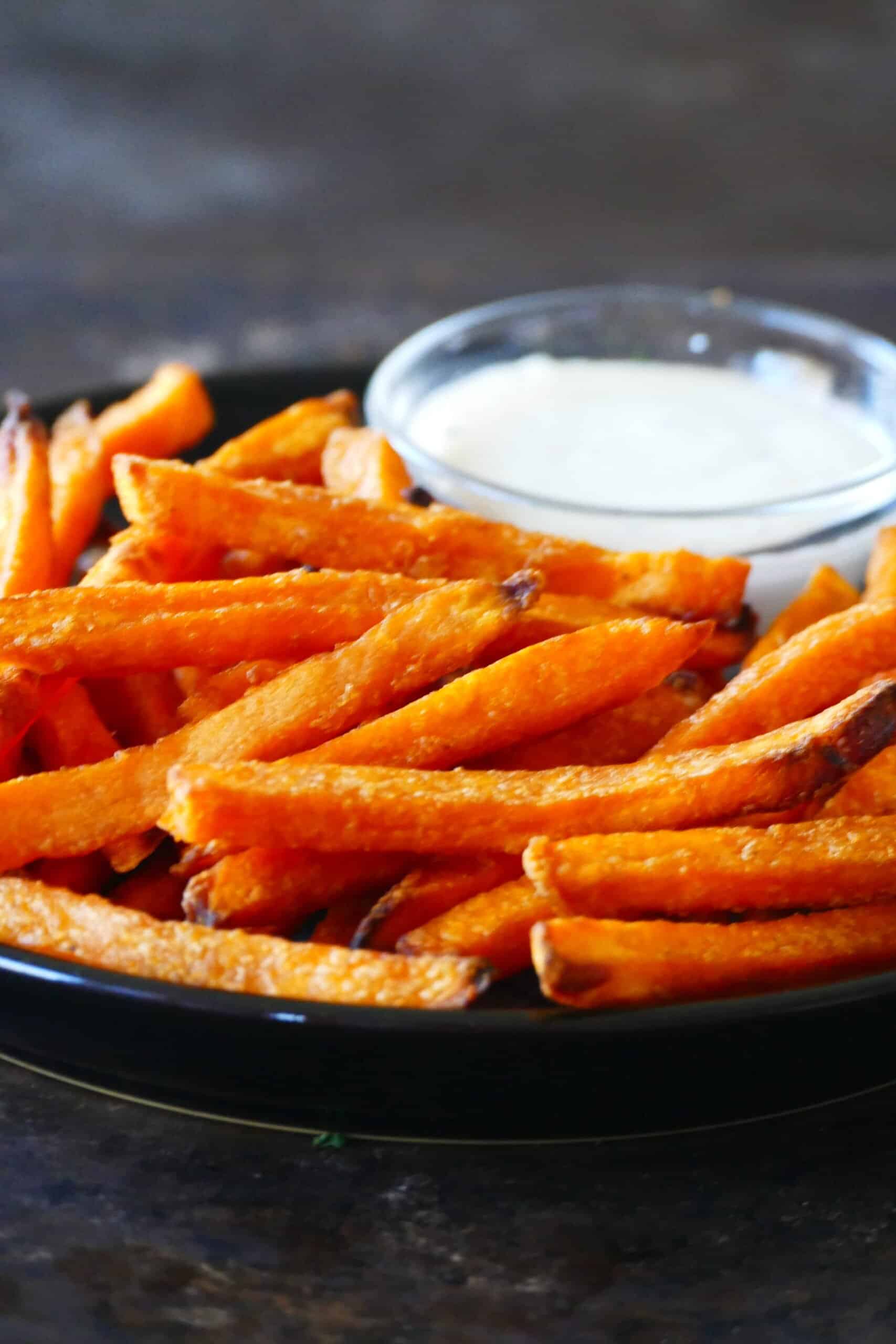 Frozen sweet potato fries in air fryer - Black plate with sweet potato fries and bowl of white sauce