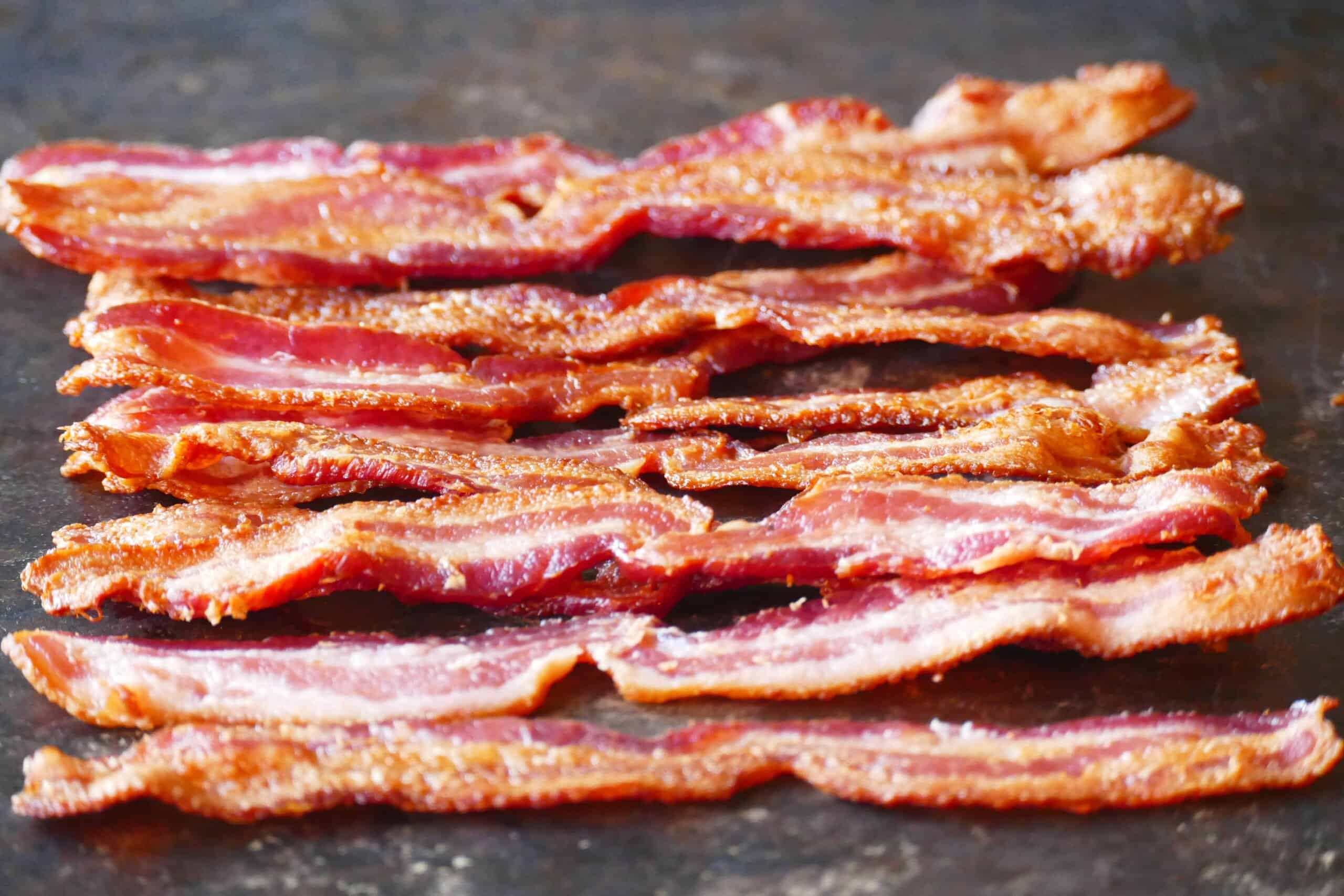 Strips of cooked bacon on black background.